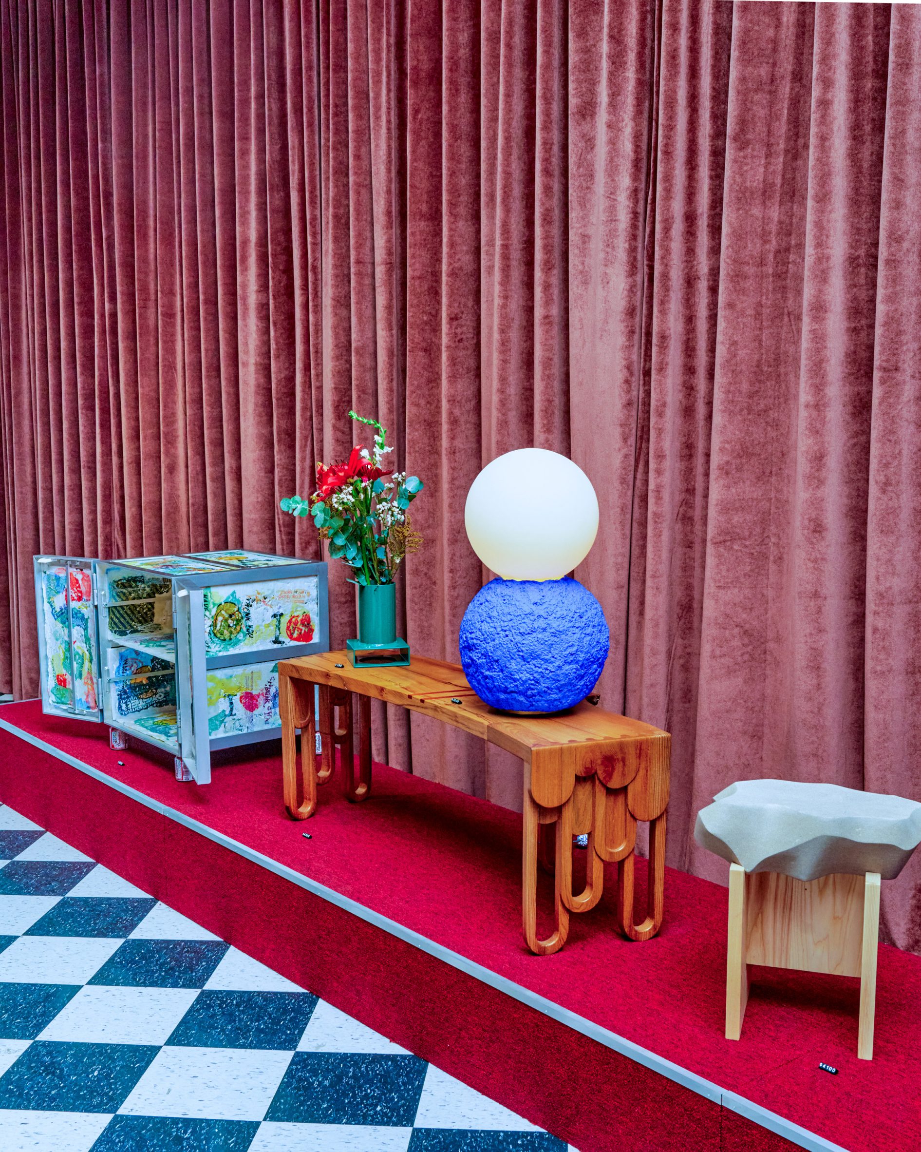 Avant-garde design pieces presented on a red plinth against velvet curtains