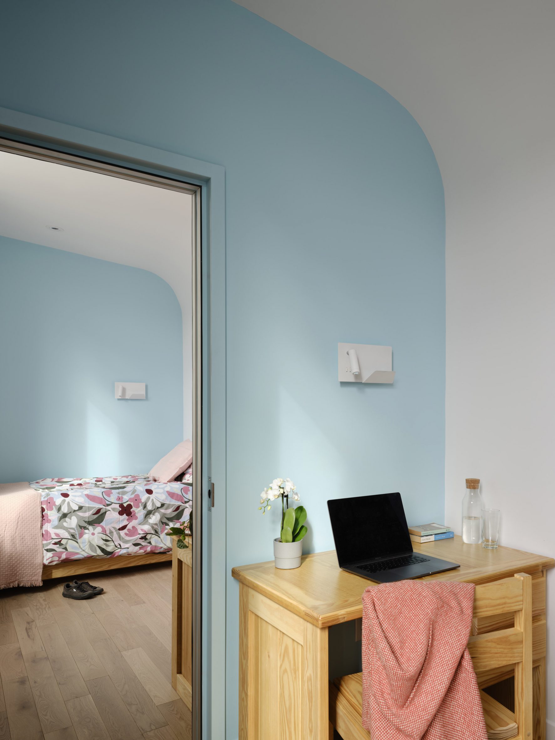 Bedroom with light blue walls, a bed and a small wooden desk