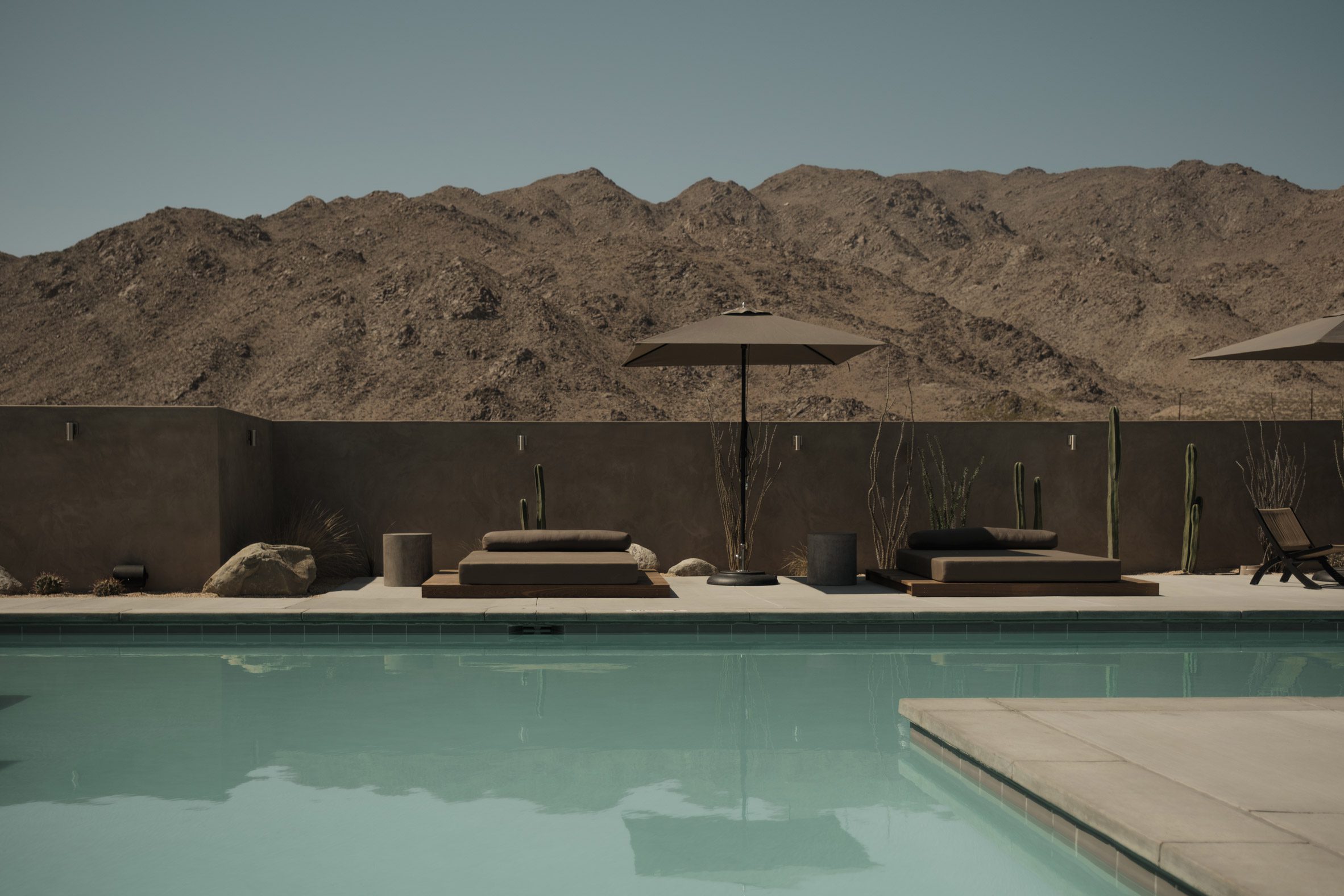 A swimming pool surrounded by loungers and cabanas, with mountains in the background